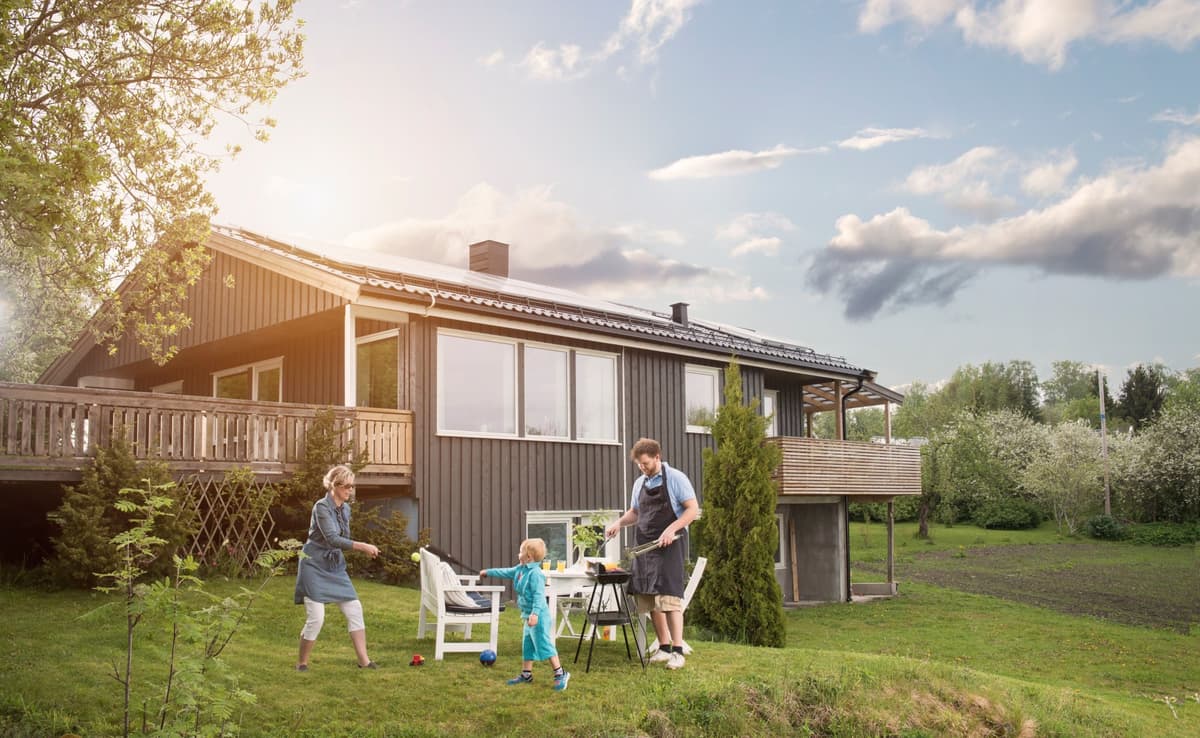 Tak med Solcellepanel En familie griller og leker i hagen foran et hus med solcellepanel på taket