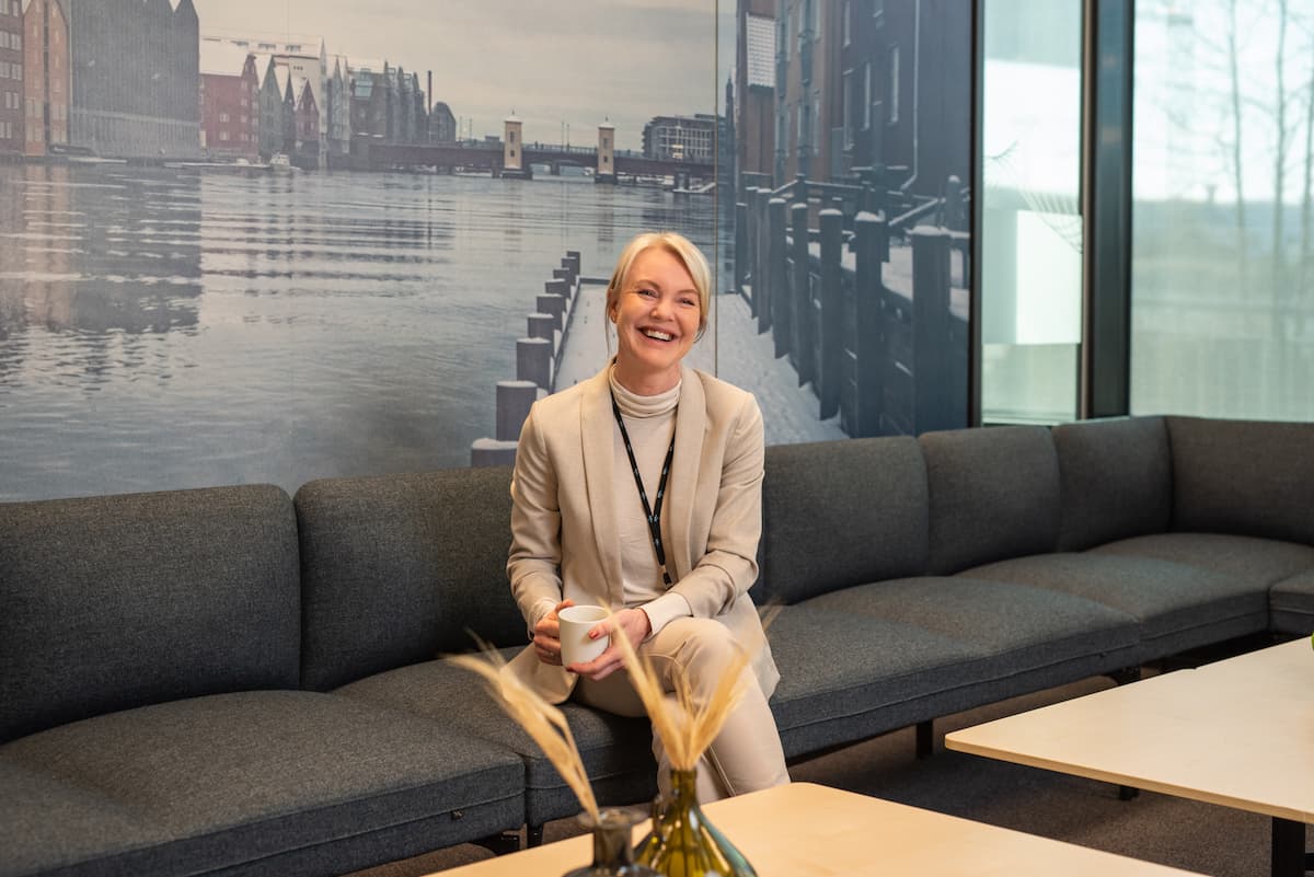 Camilla Berge Jacobsen 3 Smilende kvinne som holder en kaffekopp mens hun sitter i en sofa