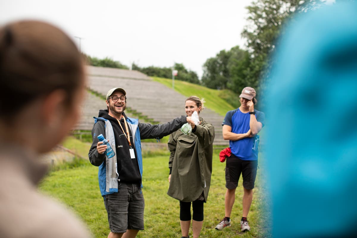 peer får dent Mann med caps holder opp en vannflaske og en liten pose mens en kvinne og en mann ser på