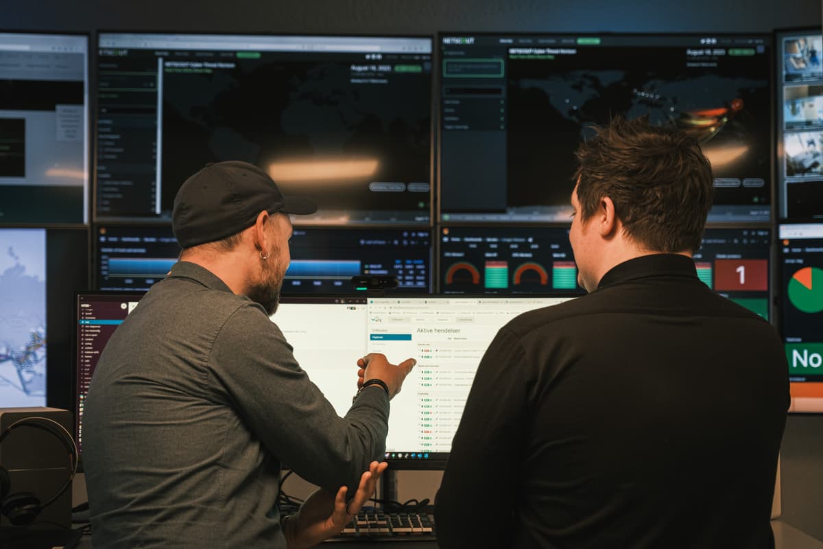 To menn står med ryggen til mens de ser på et utall dataskjermer To menn står med ryggen til mens de ser på et utall dataskjermer