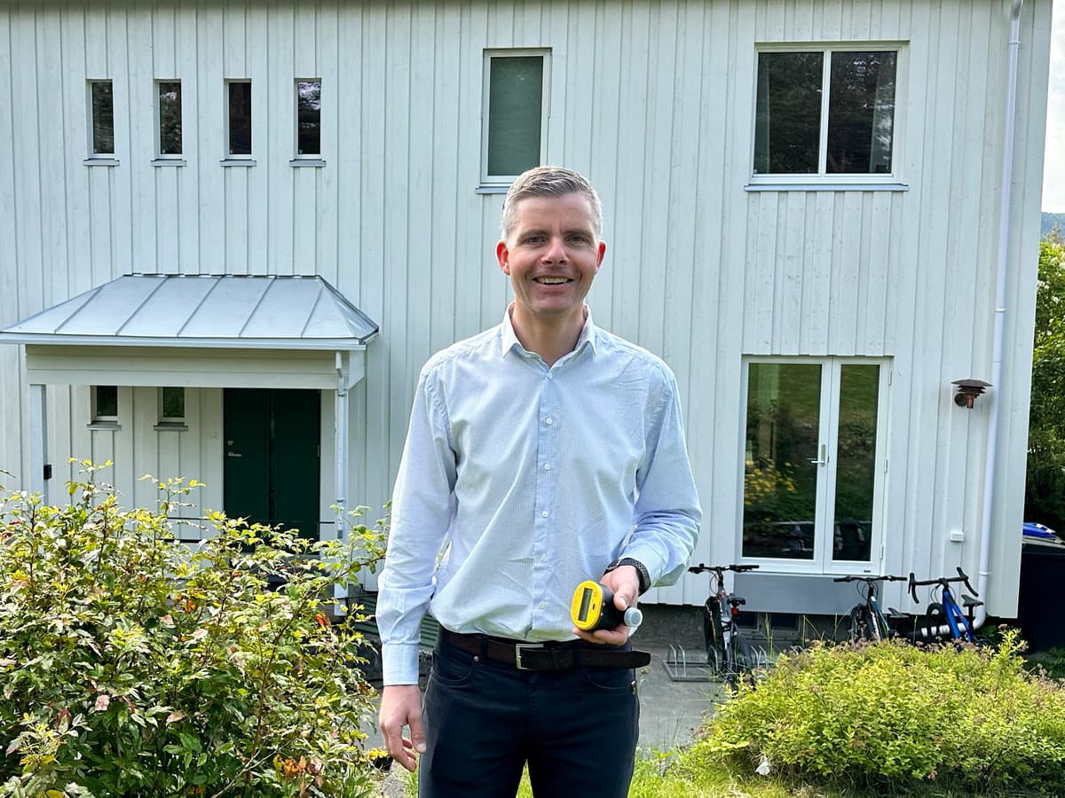 Smilende mann som holder en vannmåler i hendene står foran et bolighus Smilende mann som holder en vannmåler i hendene står foran et bolighus