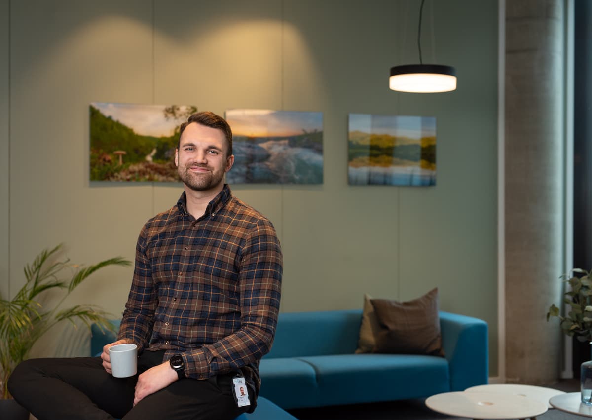 Kristian Haug Flakk Smilende mann i rutete skjorte sitter på en sofarygg og holder en kaffekopp