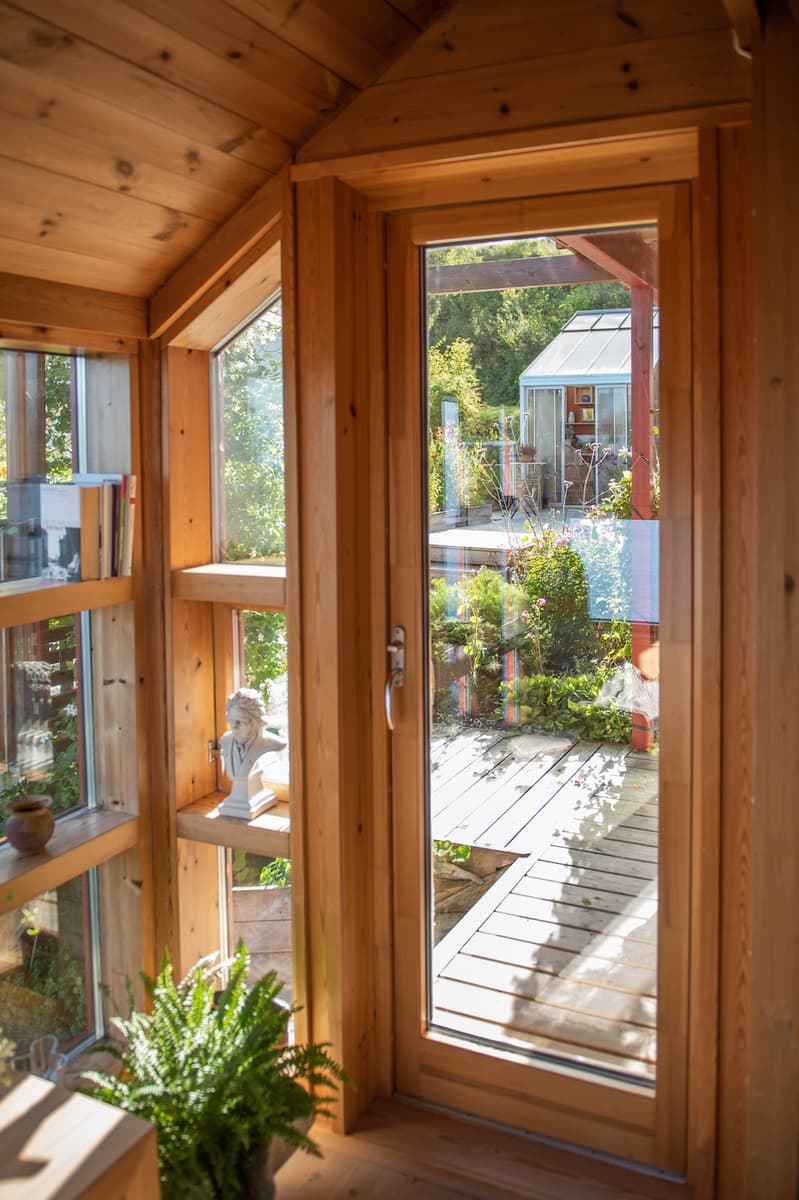 utsikt til hagen Utsikten gjennom glasset i en verandadør mot en hage med platting og drivhus