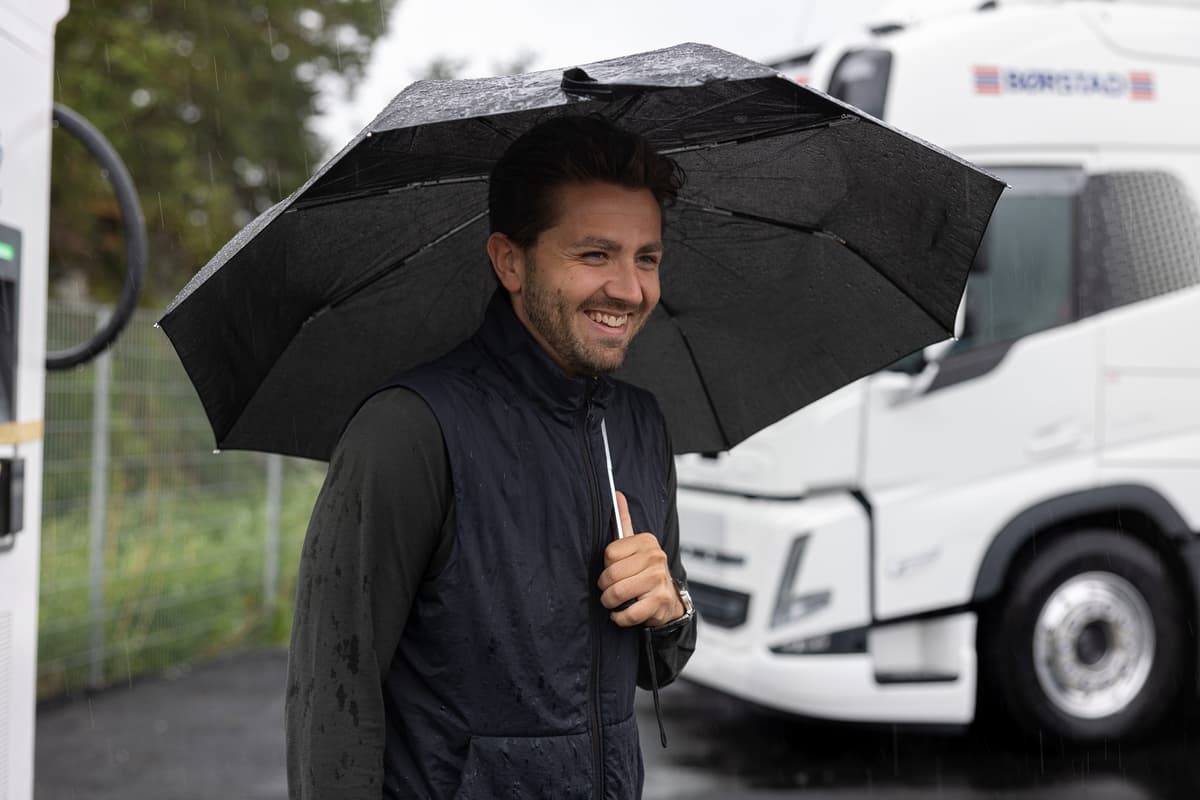 Sverre Myrvold Bjerve Smilende mann under en paraply. Bak ham står det en lastebil.