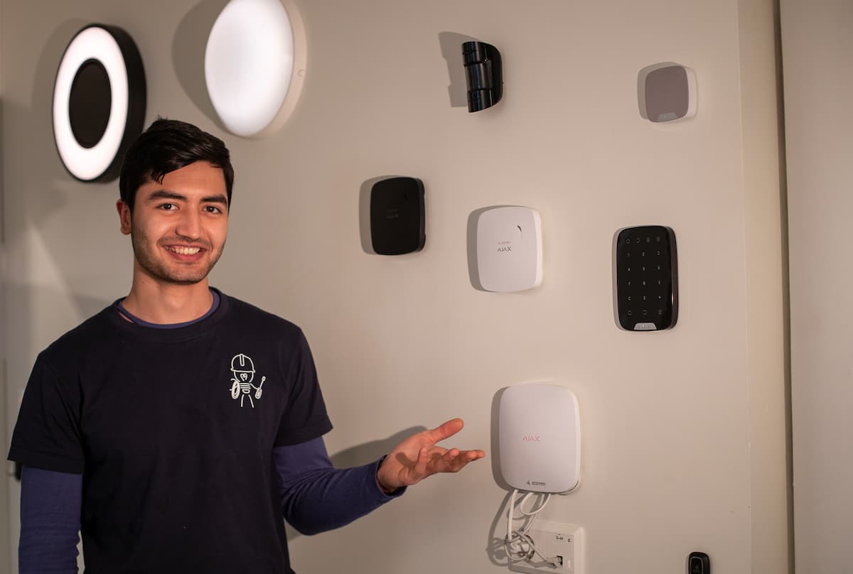 Smilende elektriker viser frem røykvarslere som henger på en vegg Smilende elektriker viser frem røykvarslere som henger på en vegg