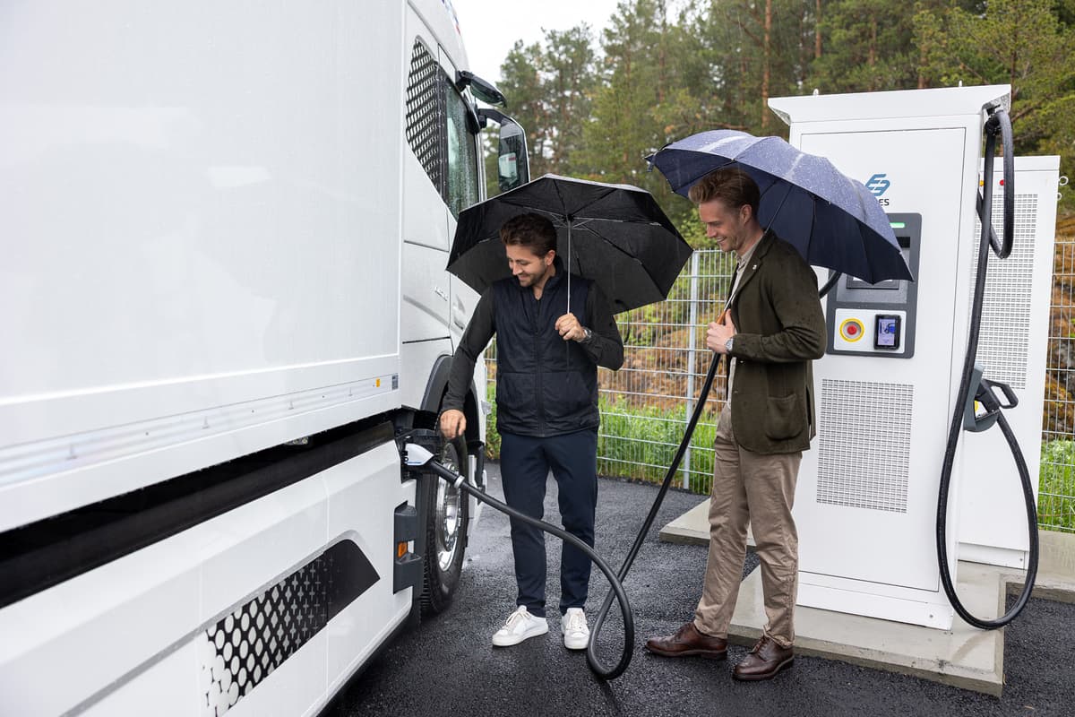Sverre og Sindre lader en elektisk lastebil To menn med paraply plugger i laderen på en elektrisk lastebil