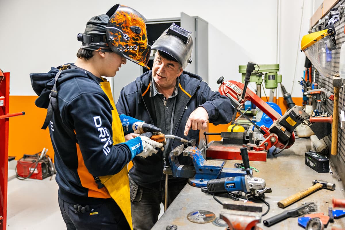 En mann lærer en ungdom å sveise ved en arbeidsbenk. Foto. En mann lærer en ungdom å sveise ved en arbeidsbenk. Foto.
