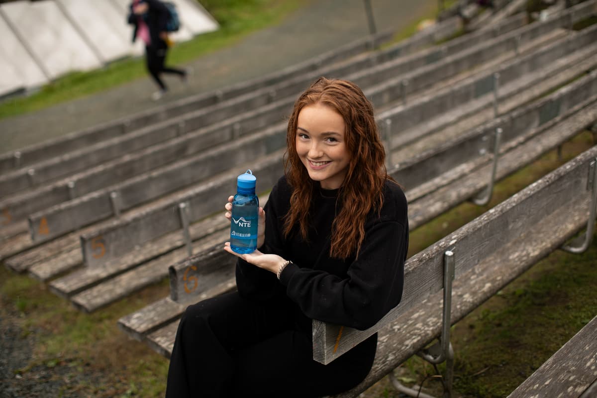 Lisa Tuset Storhaug Smilende jente sitter på en benk og holder i en vannflaske