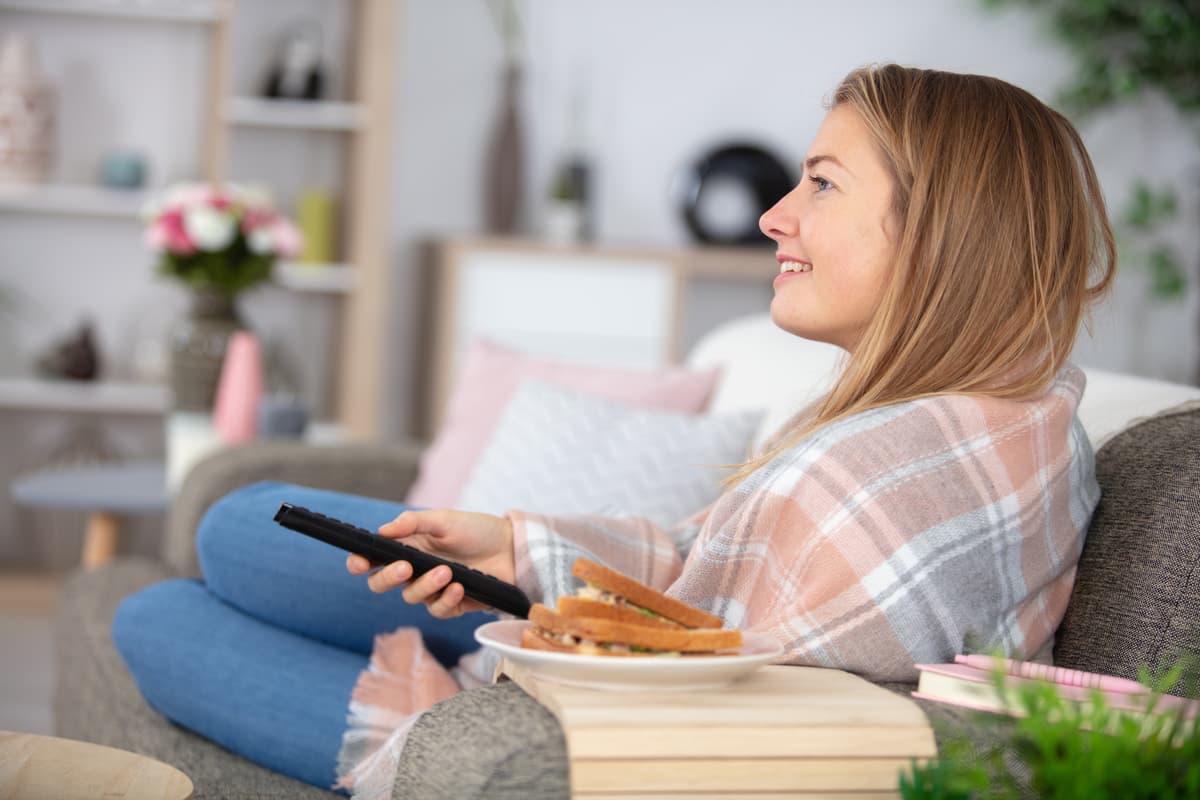 dame ser tv dame ligger i sofaen og ser tv med en brødskive på bordet ved siden av seg