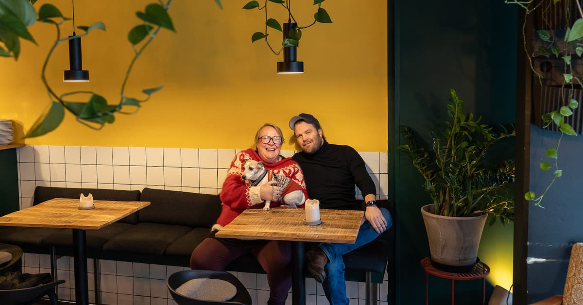 Marit Gjeset og Lornts Tønne Smilende kvinne og mann sitter ved et kafébord med en hund mellom seg
